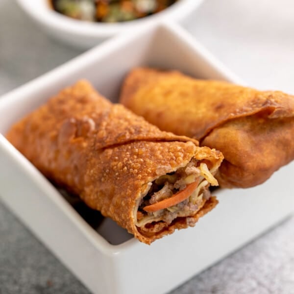 2 gluten free egg rolls in egg roll wrappers in small square white dish with bite taken from one