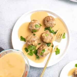 5 gluten free Swedish meatballs with tan gravy on white plate with gold fork