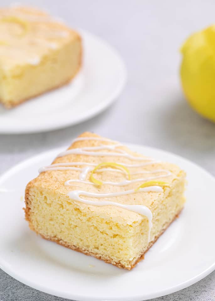 Lemon brownie with icing drizzle and some lemon zest on small white plate