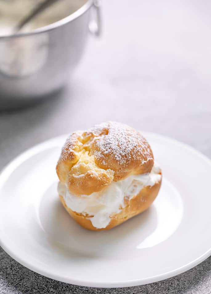 One cream-filled choux pastry on small white plate with confectioners sugar on top