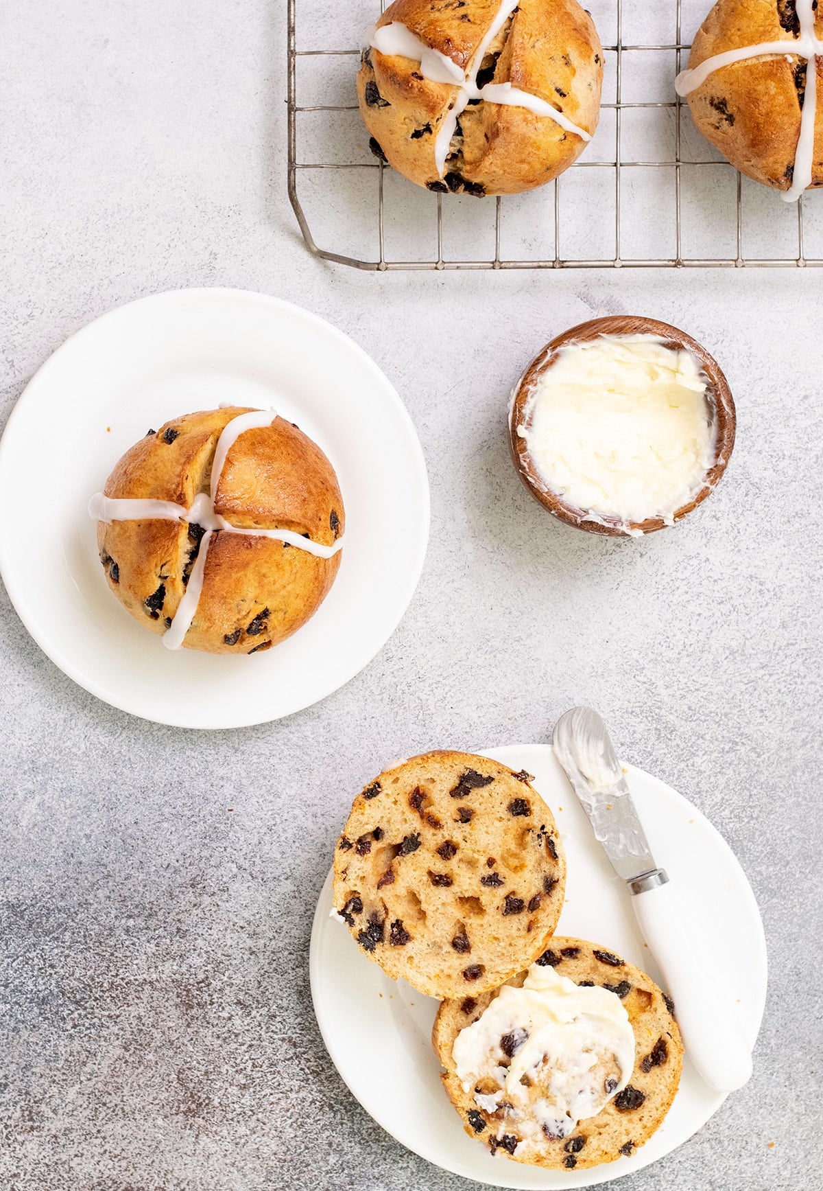 Overhead image of hot cross buns on wire rack, on small plate, and on small plate cut in half with butter