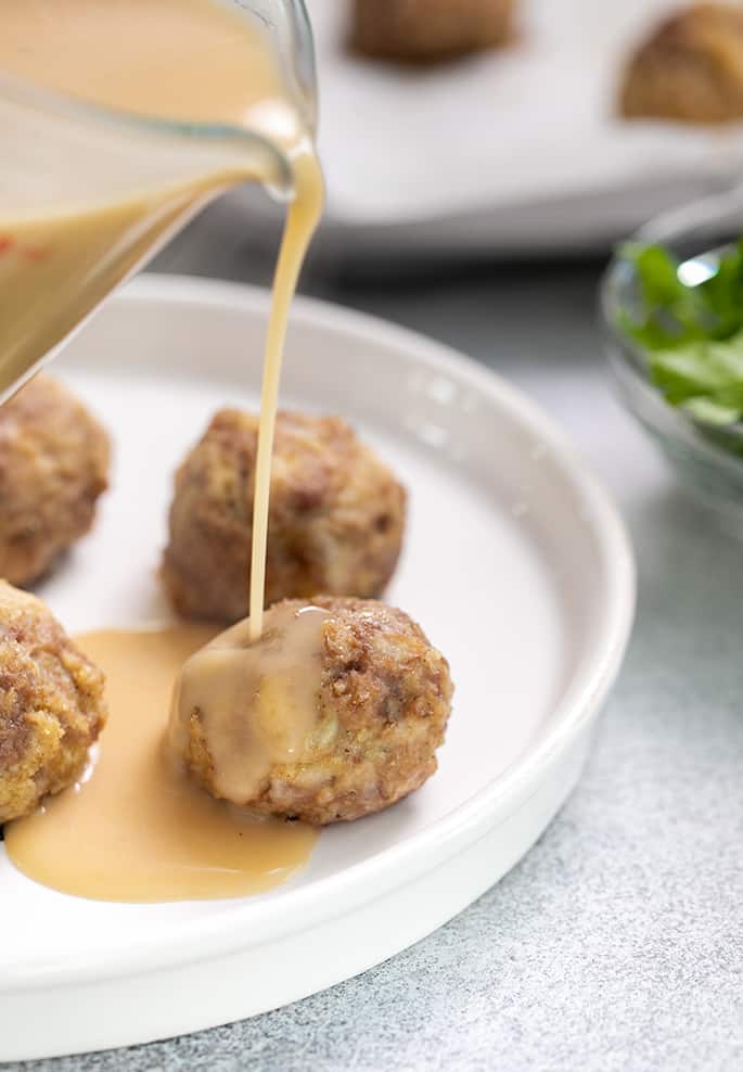 Swedish meatball gravy being poured onto meatballs on white plate