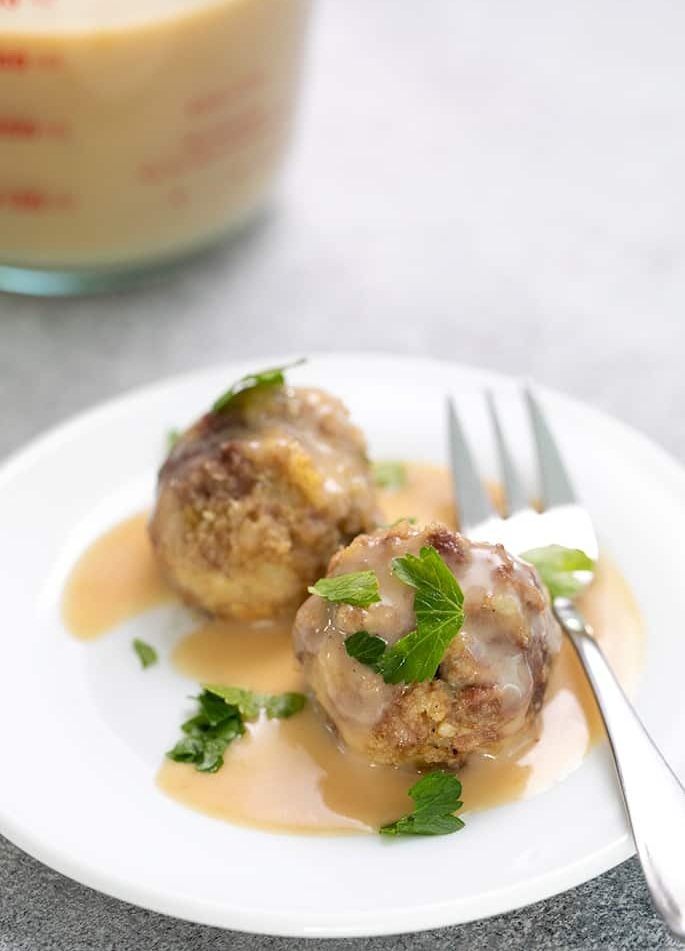 two gluten free Swedish meatballs with parsley and gravy on a small white plate with a small appetizer fork