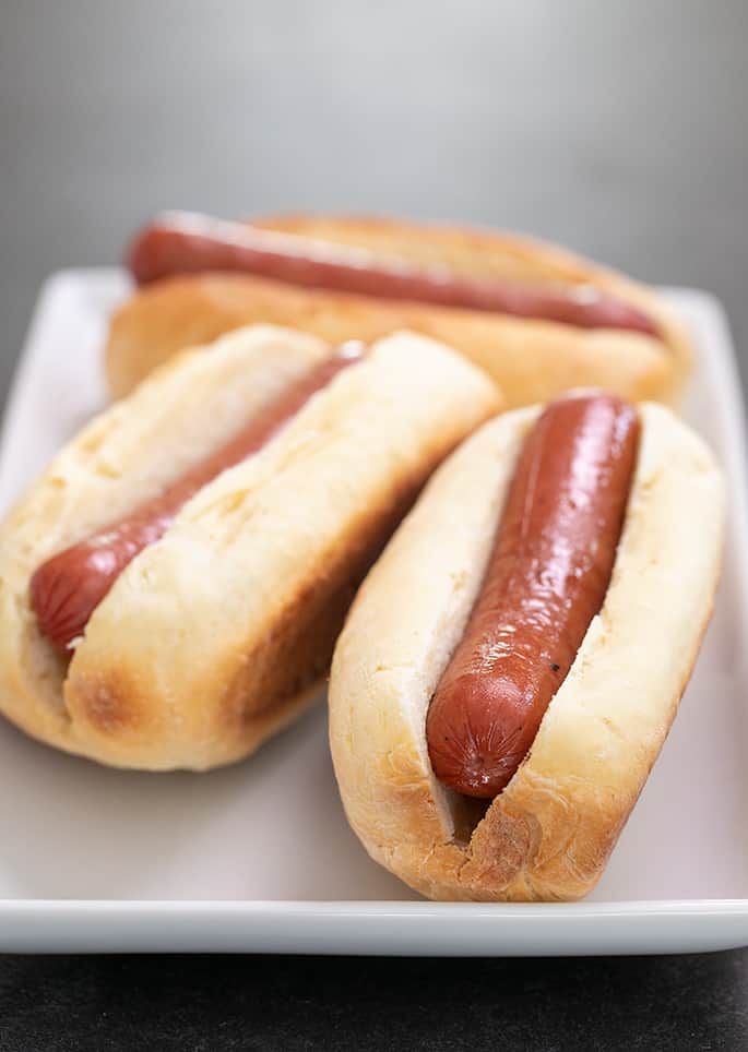 White rectangular plate with 3 hot dogs in buns