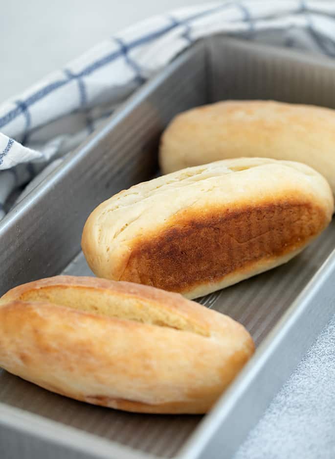 hot dog buns in rectangular metal pan with blue and white checked tea towel