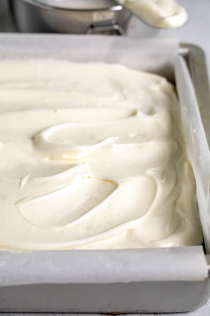 Closeup image of white frosted cake in square metal dish with more frosting in background