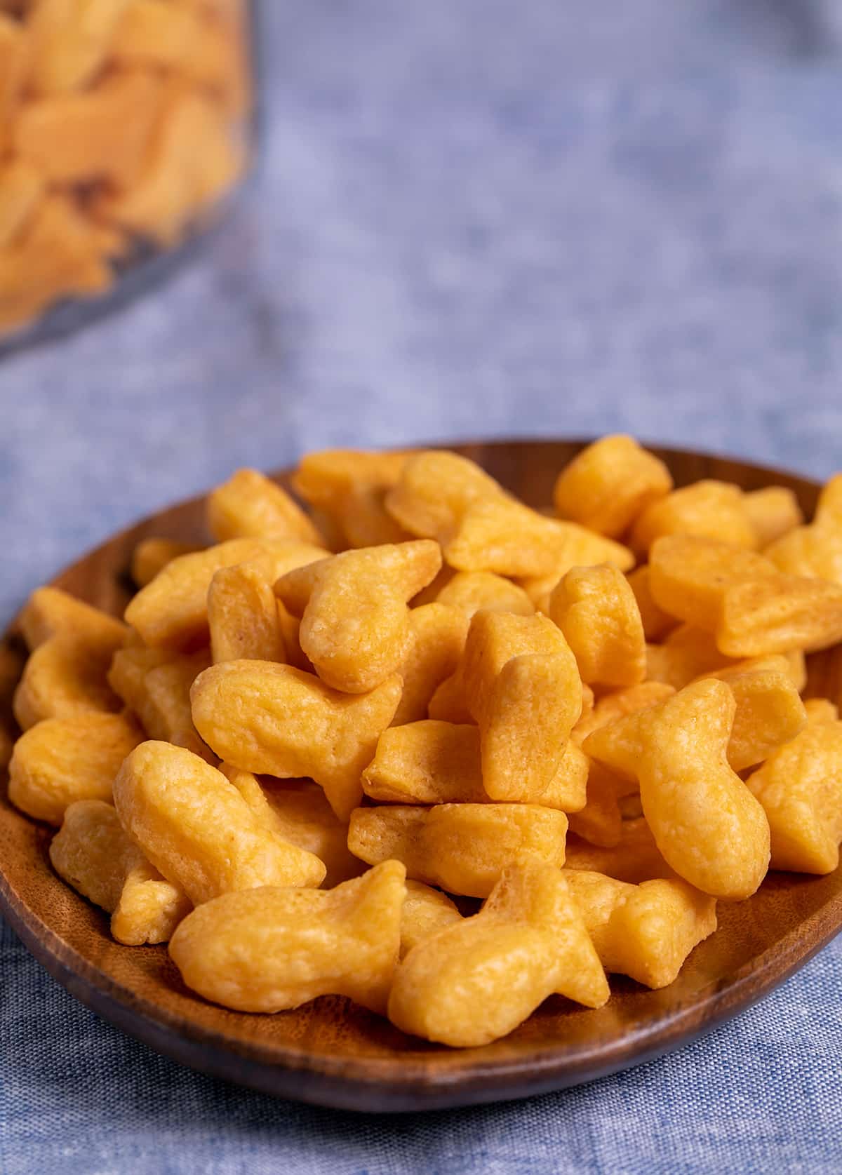 Goldfish shaped crackers in a pile on a small brown acacia plate on blue cloth