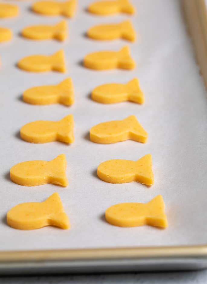 Raw goldfish-shaped cracker dough cutouts on white paper on tray