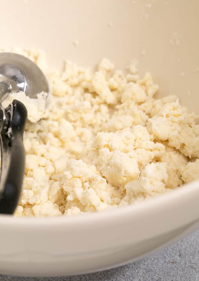 Raw unformed biscuit dough with ice cream scoop in large mixing bowl