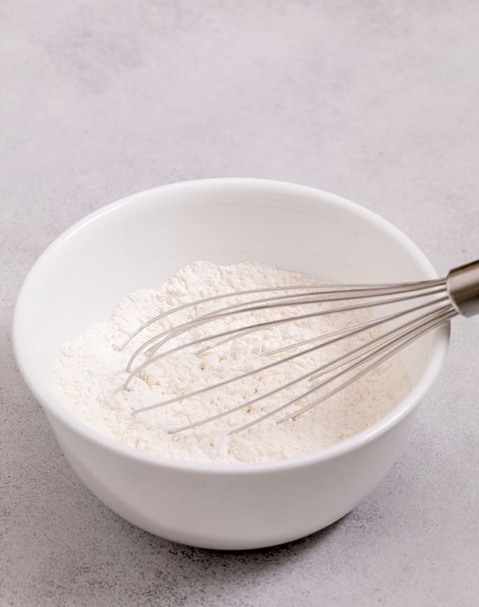 Small white bowl with flours and a large whisk