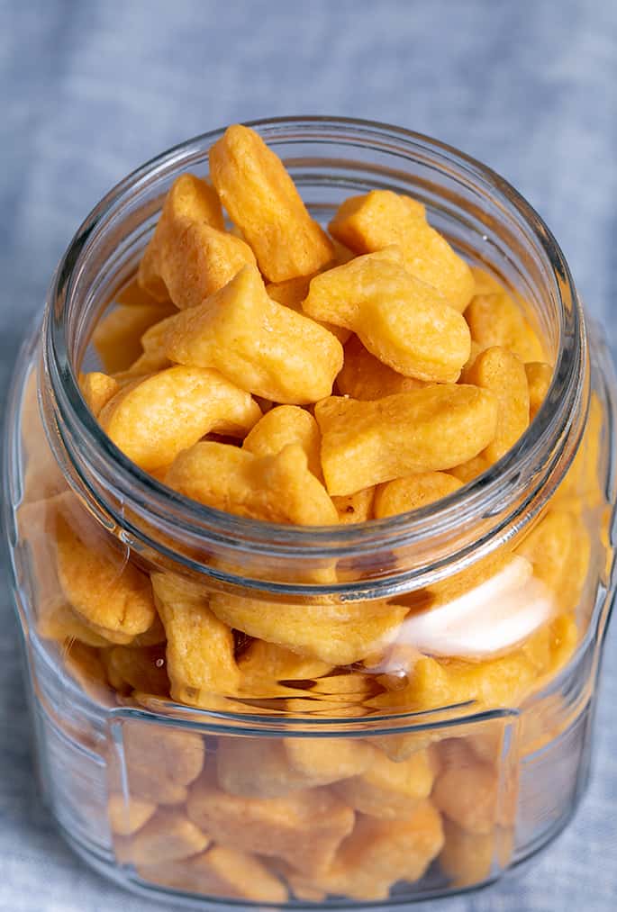 Square glass jar filled with goldfish-shaped crackers on blue cloth