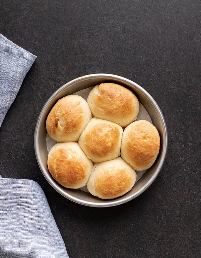 Overhead image of 6 baked gluten free dinner rolls in round baking dish