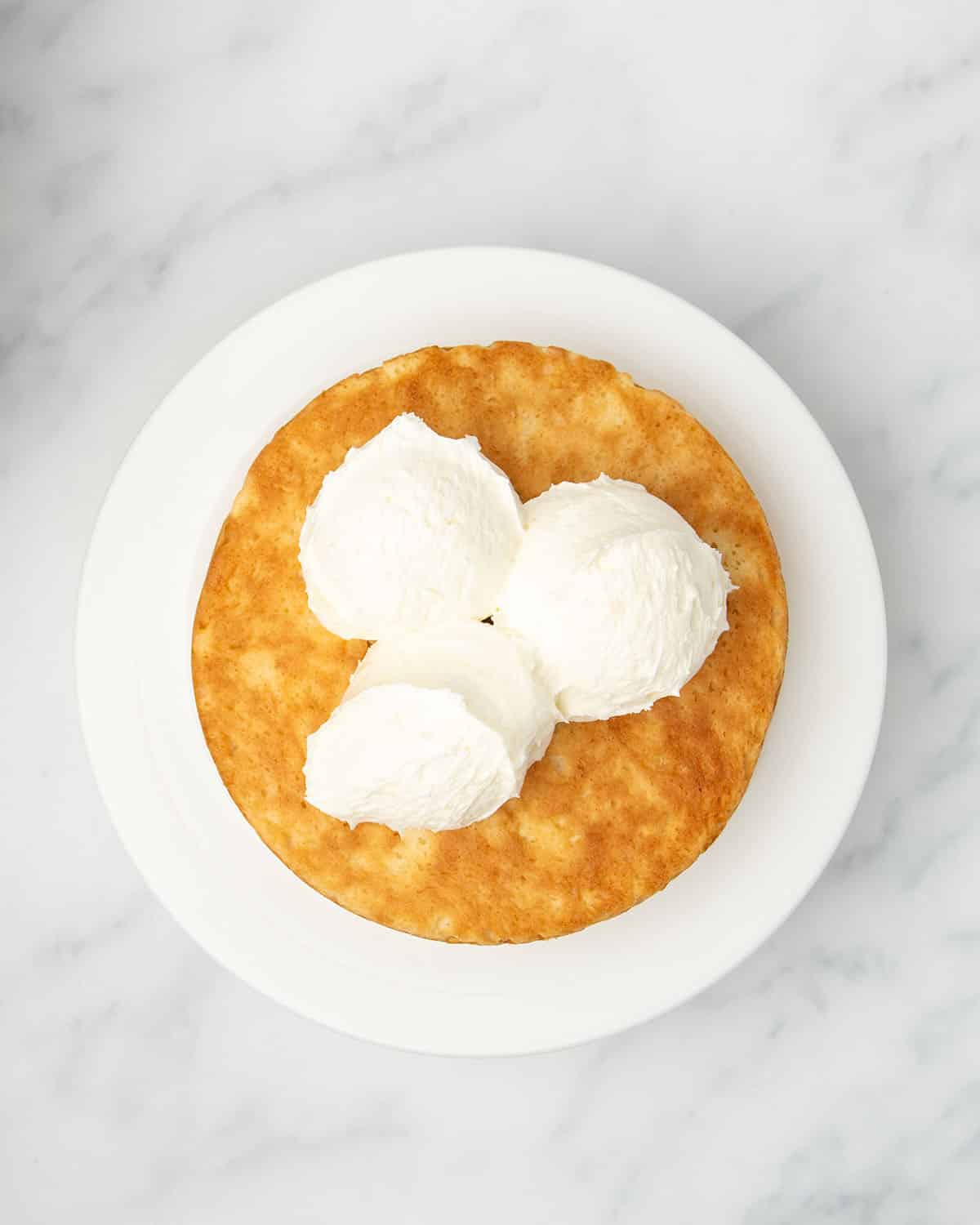 Round yellow and brown baked cake with 3 scoops of white frosting on white plate