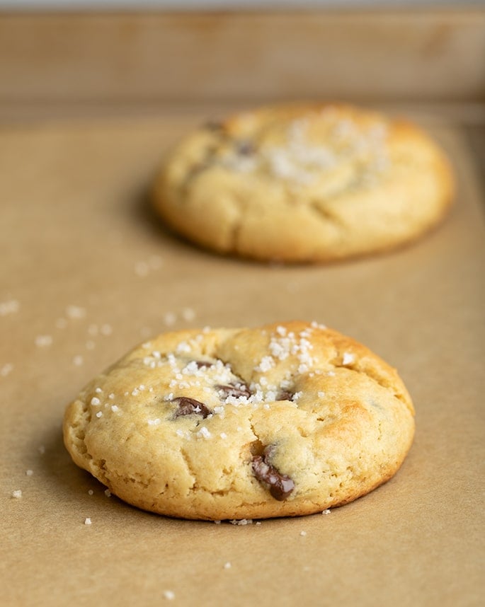 Two baked chocolate chip cookies with salt on brown paper on tray