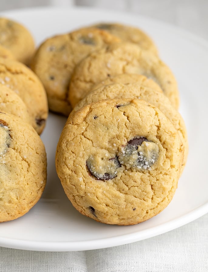 Two rows of chocolate chip cookies lined up on a large white round platter on a white cloth