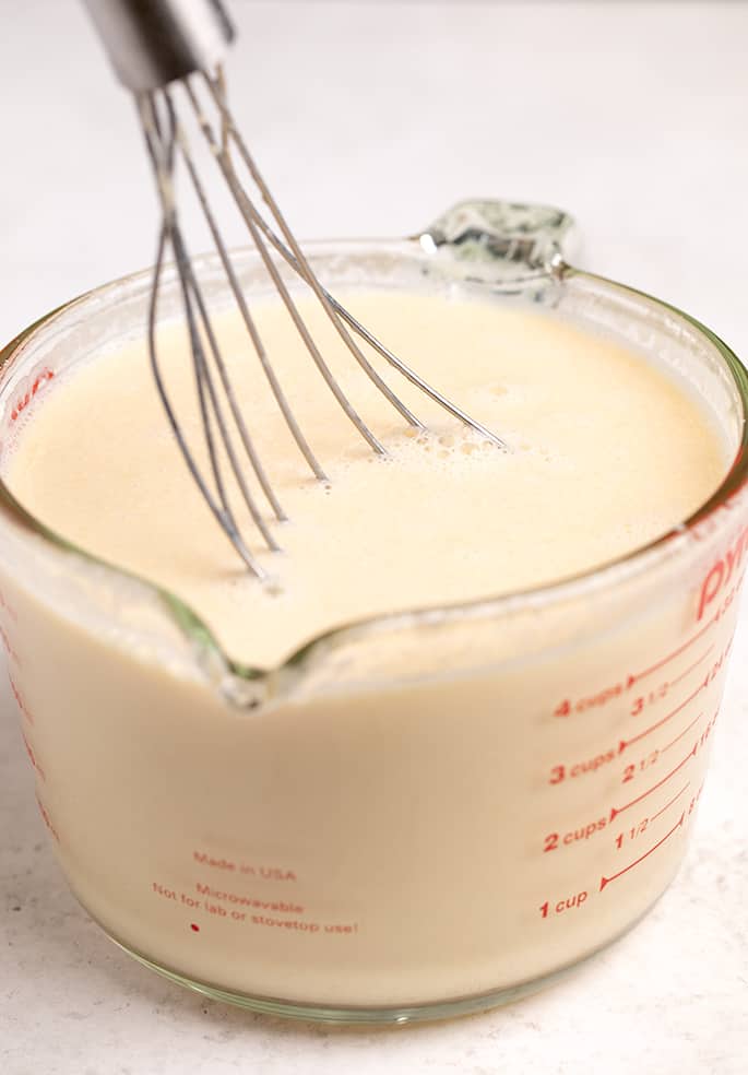 4 cup pyrex measuring cup filled with tan liquid with a flat whisk on white table