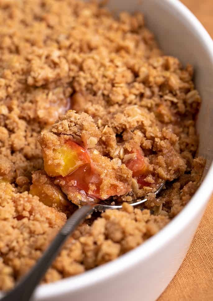 Closeup image of serving spoon in white serving dish of peach crisp