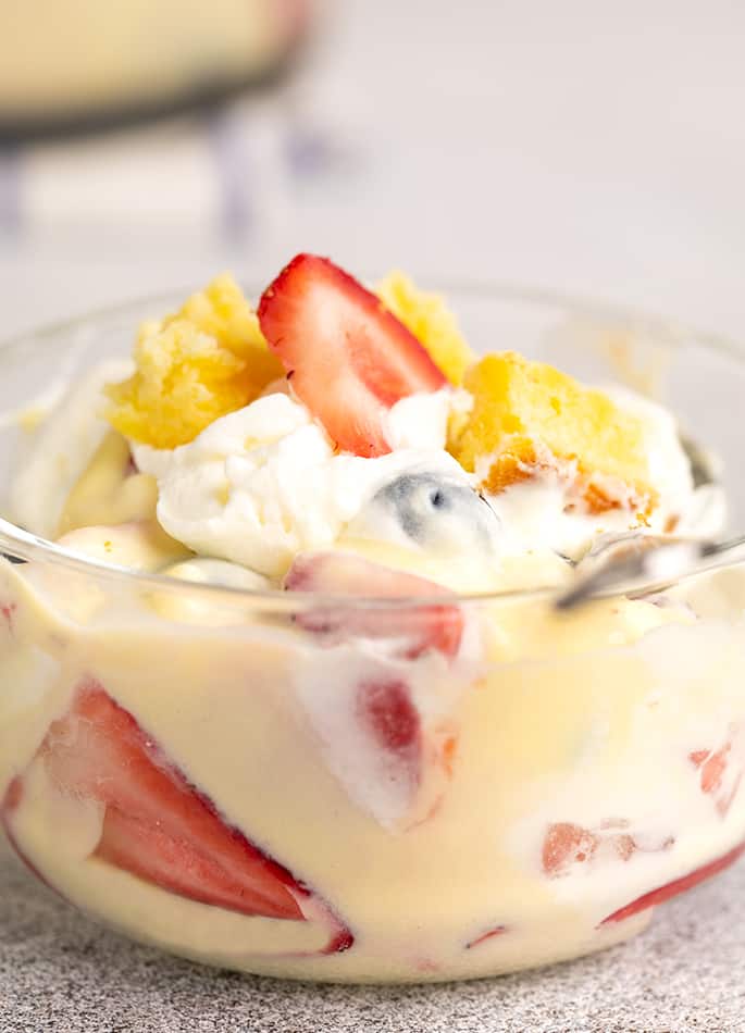 Custard, pound cake, strawberries, and whipped cream in small glass bowl with spoon