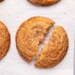 closeup image of light brown gluten free snickerdoodle cookie on white paper lined baking sheet broken in half