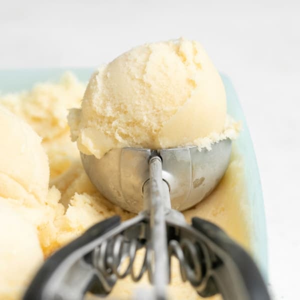 yellow scoop of vanilla ice cream made without cream in a metal ice cream scooper in a green container