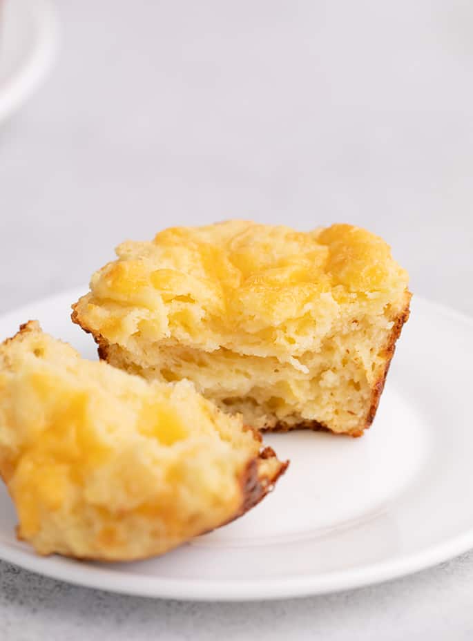 Muffin torn in half on small white plate on white table