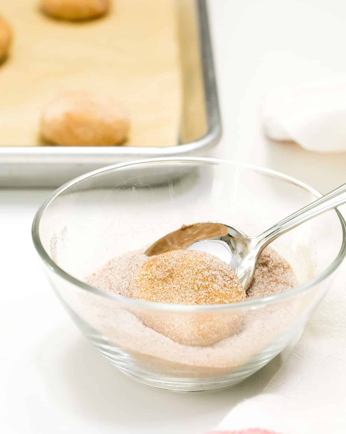 disk of gluten free snickerdoodle cookie dough in glass bowl with cinnamon sugar mixture and spoon