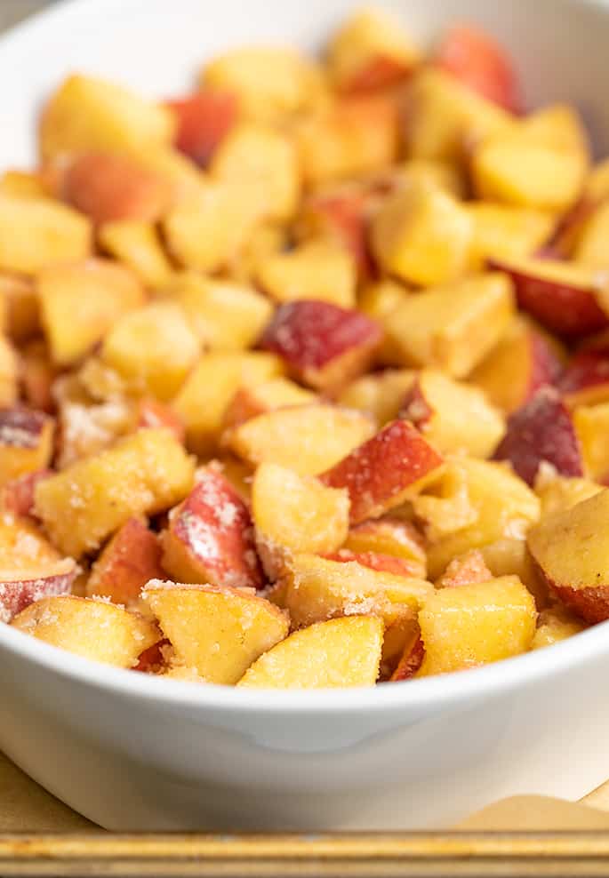 Raw chunks of peaches in oval white baking dish on metal tray for gluten free peach crisp