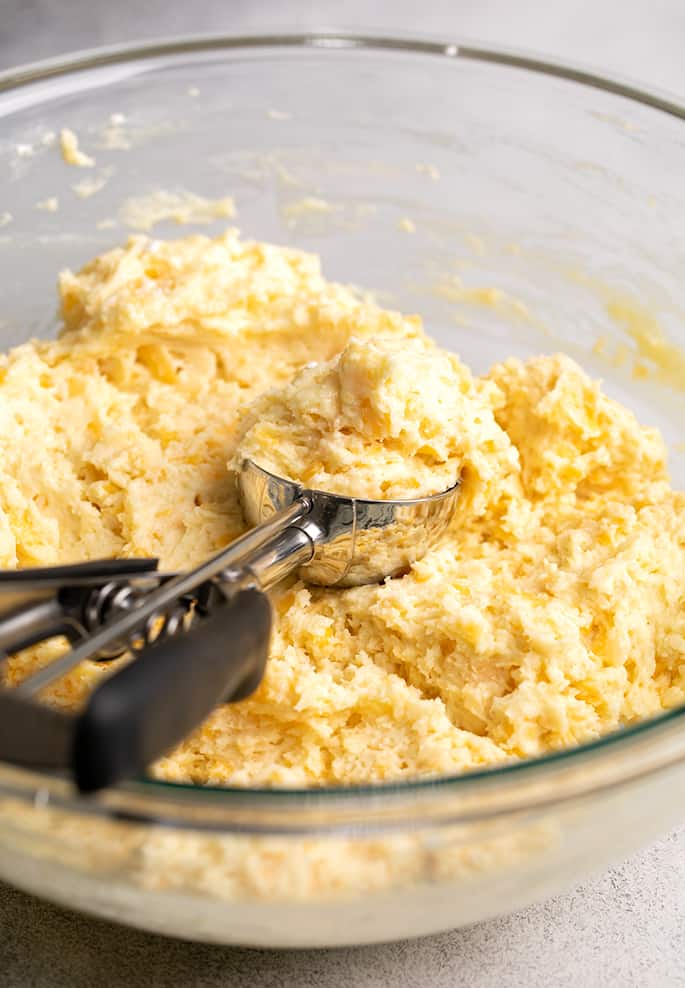 Raw muffin batter in large glass bowl with spring loaded ice cream scoop