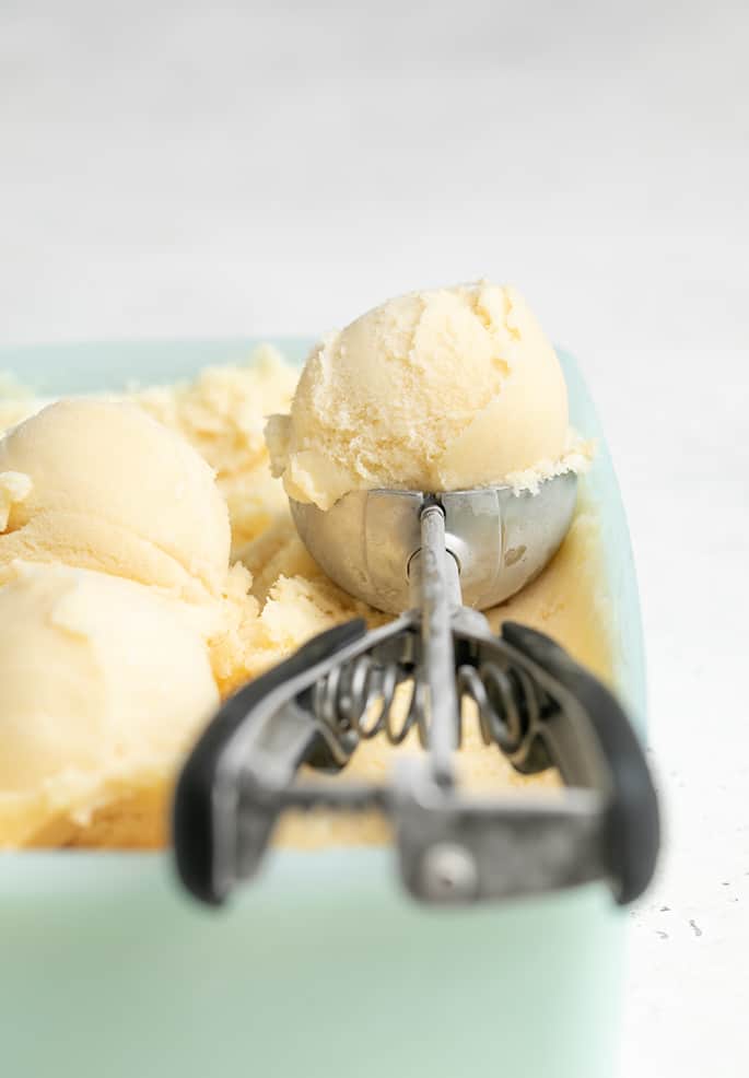 Vanilla ice cream in a green freezer container with more ice cream