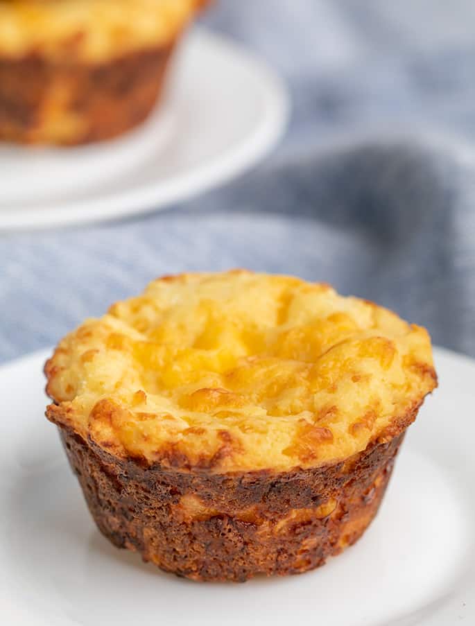 Whole baked muffin in foreground on small white plate with second muffin on white plate in background