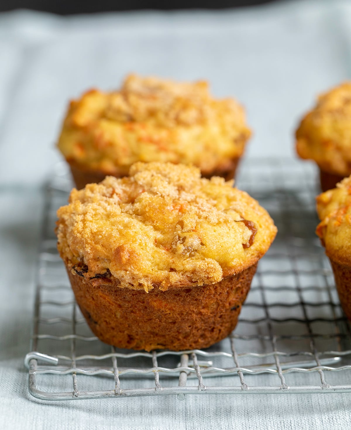 4 carrot muffins on a wire rack on a light blue cloth