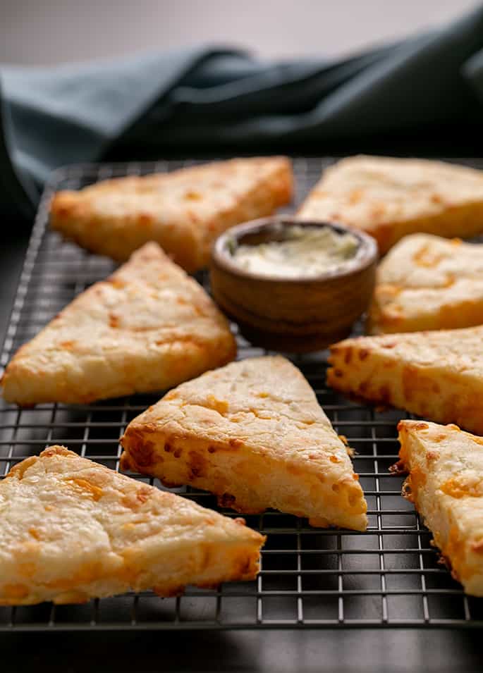 Cheese scones on wire rack on black surface with blue cloth in background