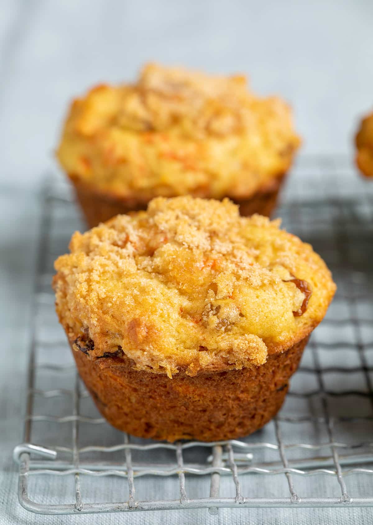 Closeup image of carrot muffin on wire rack on light blue cloth