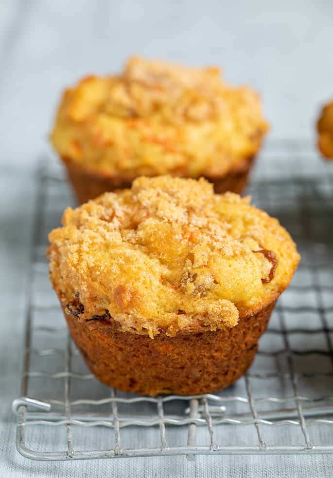 Closeup image of carrot muffin on wire rack on light blue cloth