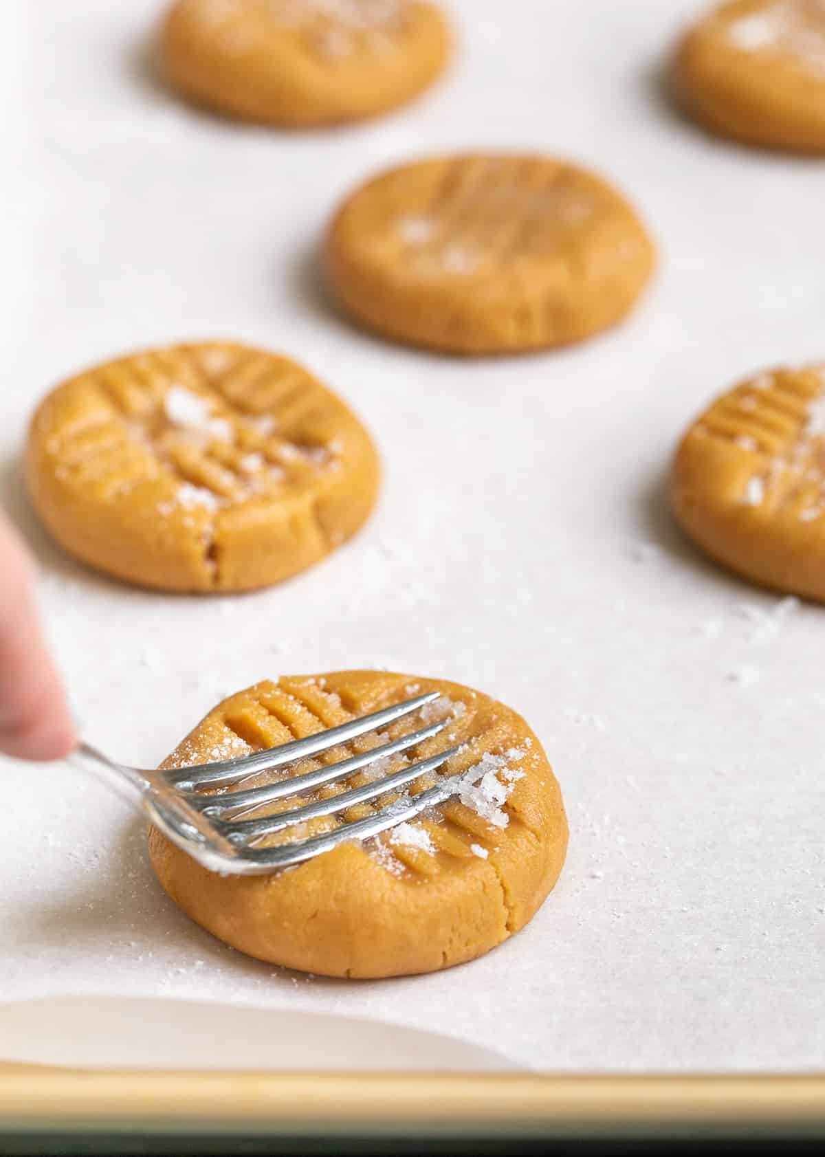 Finger pressing tines of fork into disk of raw gluten free peanut butter cookie dough