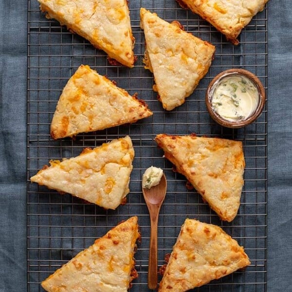 Overhead image of 8 cheese scones with butter on wire rack on blue cloth