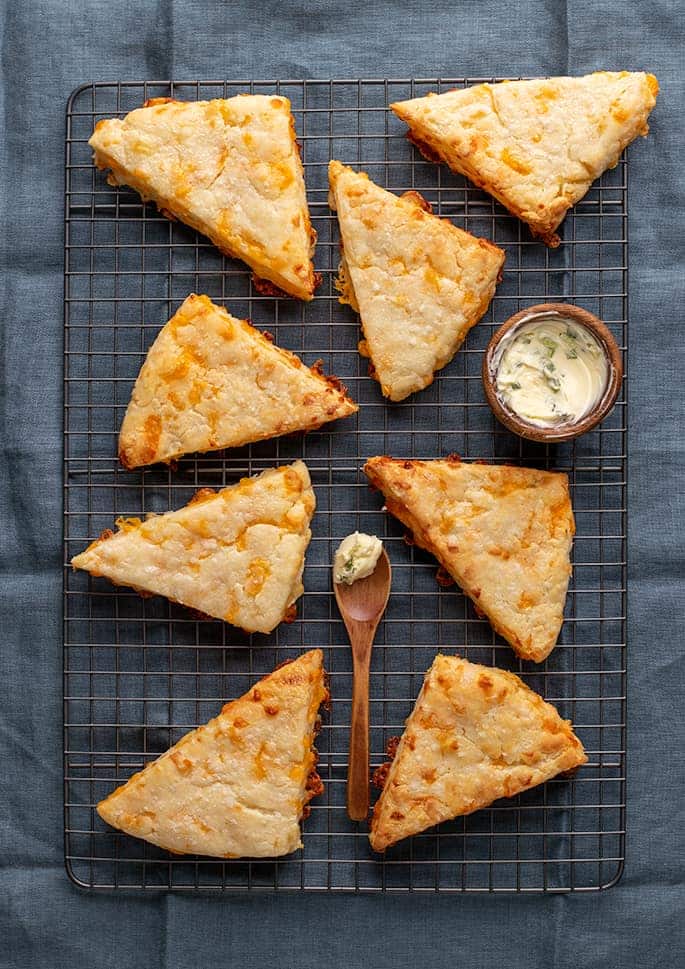 Overhead image of 8 cheese scones with butter on wire rack on blue cloth