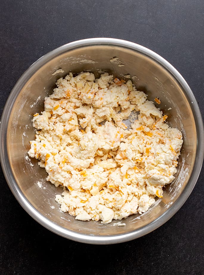 Overhead image of cheese scone dough in metal bowl on black surface