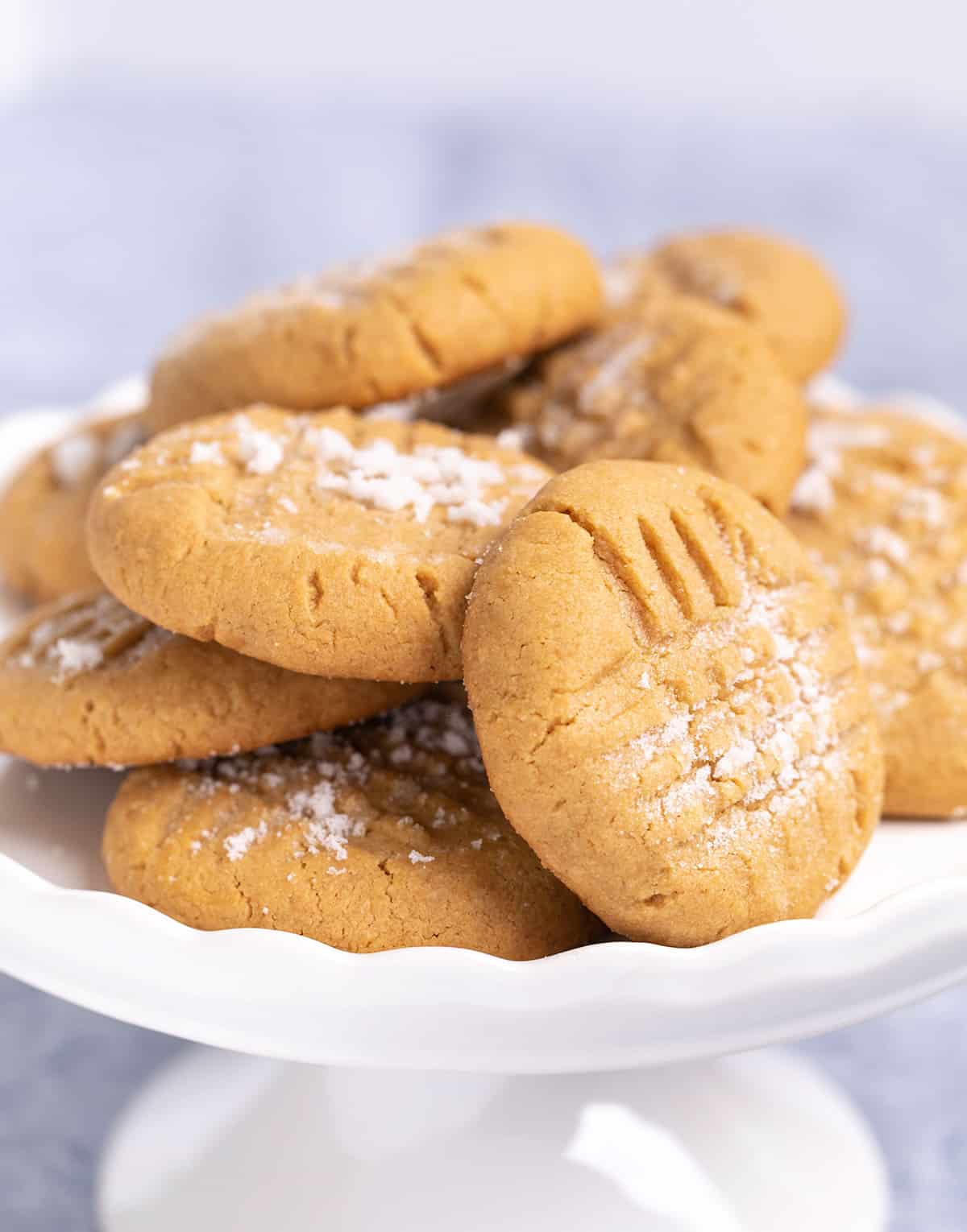 Pile of peanut butter cookies on small white cake plate on blue cloth