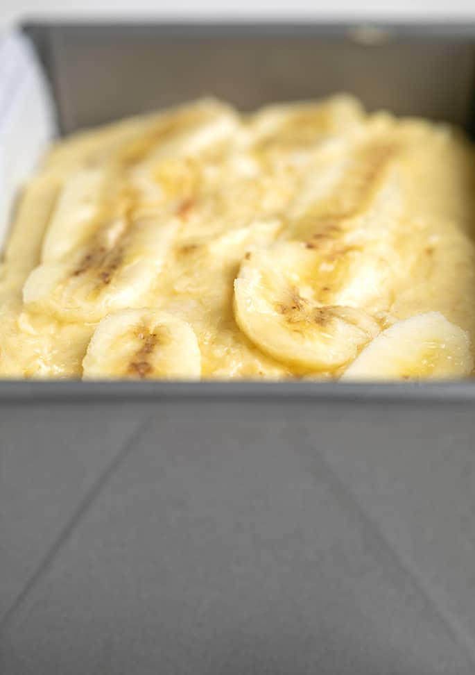 Raw gluten free banana bread batter with thin sliced bananas on top in metal loaf pan