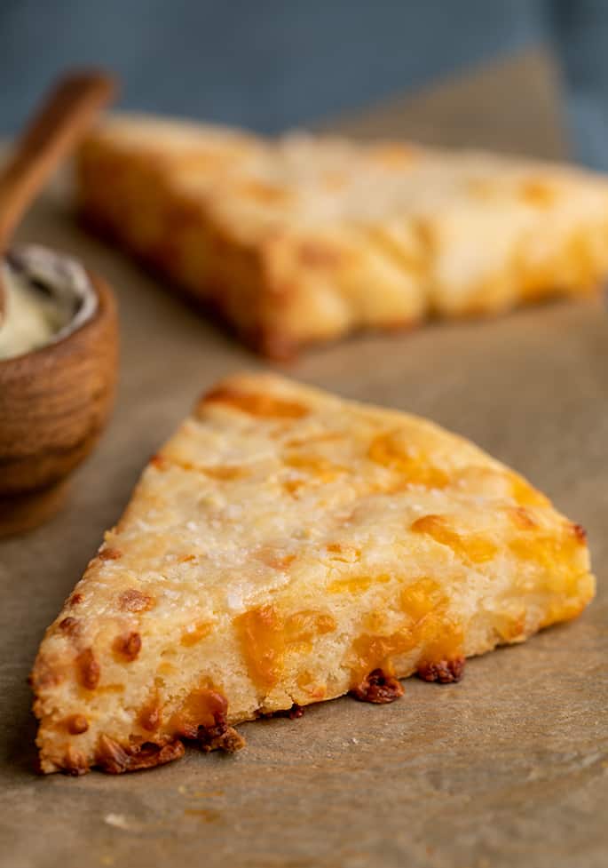 Two cheese scones on brown parchment paper with a wooden bowl and spoon