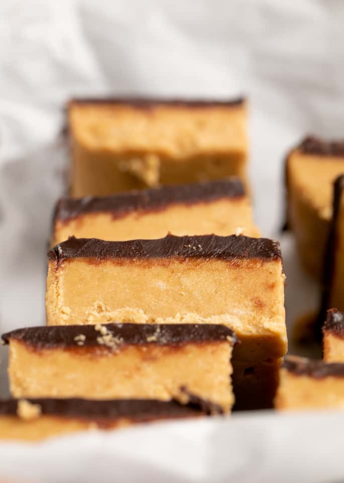 Closeup image of chocolate topped peanut butter bar squares stacked on their side on white paper