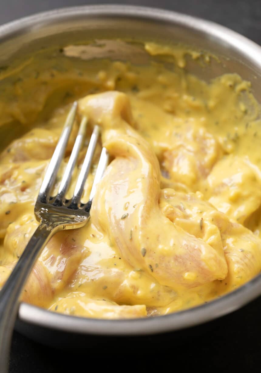 fork in round metal bowl filled with raw chicken strips in yellow batter