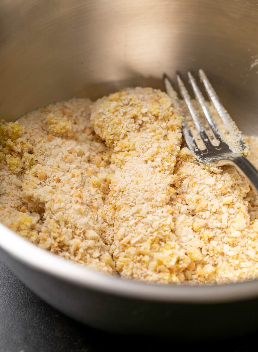 fork with chicken strips coated in coarse bread crumbs in round metal bowl