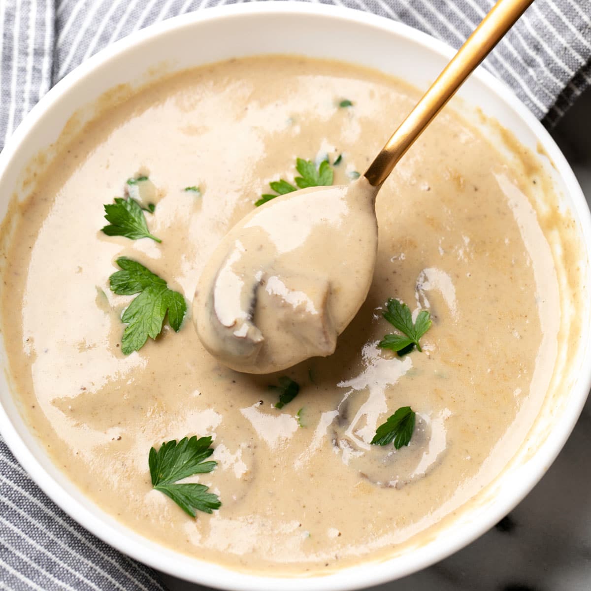 gluten free cream of mushroom soup in white bowl with spoonful on striped cloth