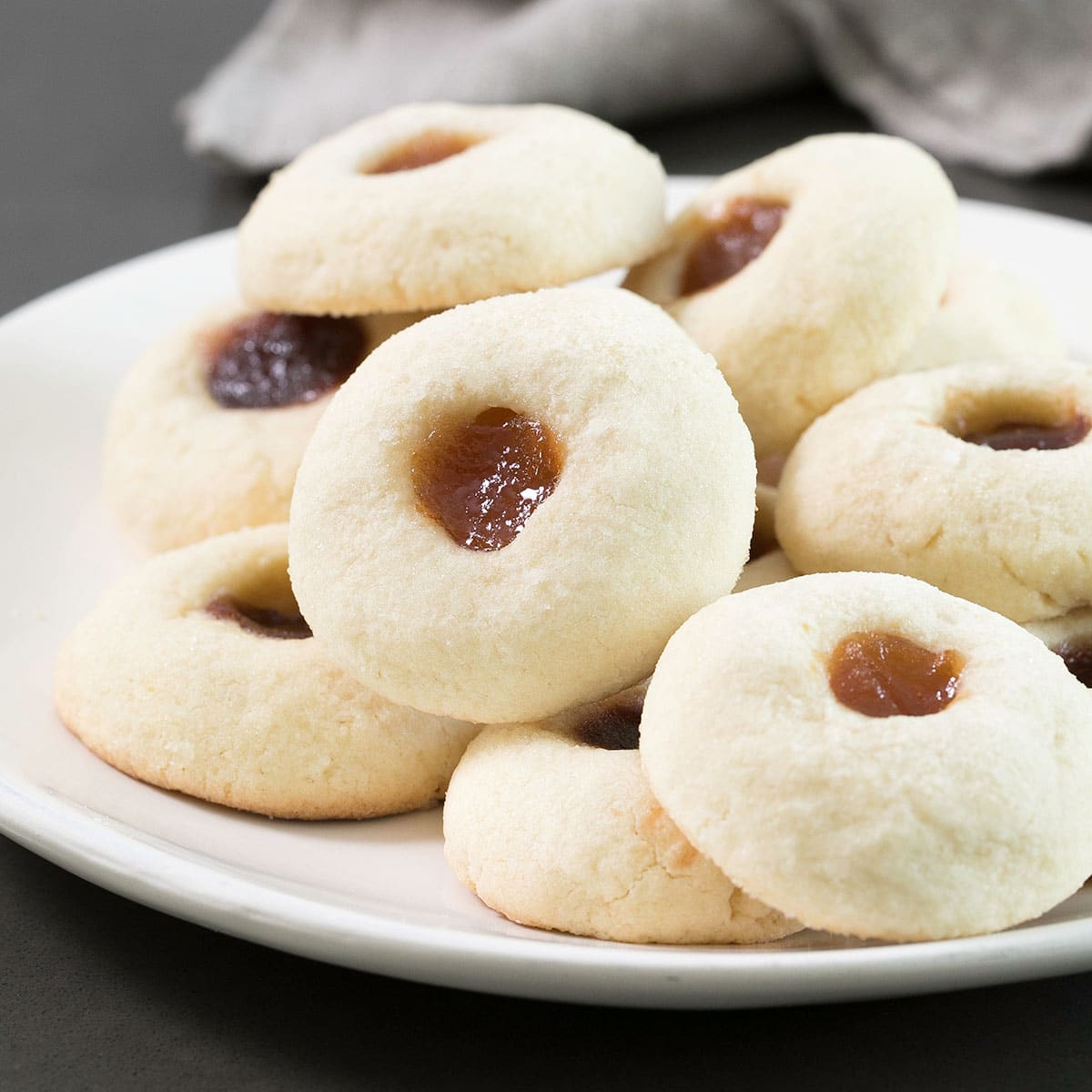 gluten free thumbprint cookies with jam in the center in a pile on a white serving plate