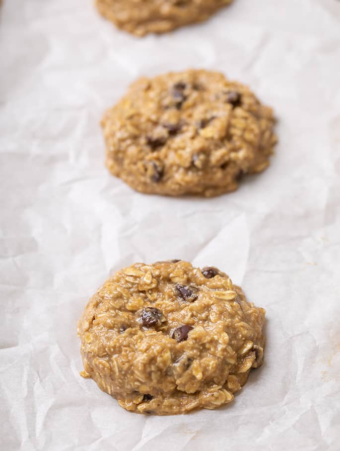 two mounds of pale brown raw oatmeal cookie dough on white parchment paper