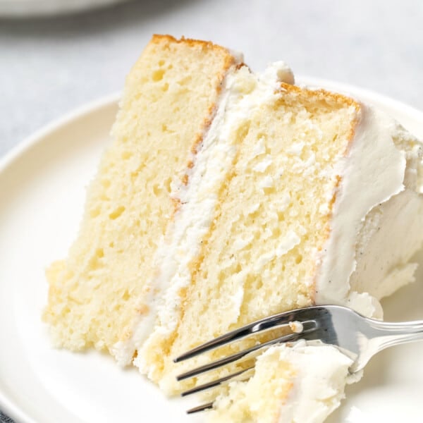 slice of 2 layer gluten free vanilla cake with white buttercream frosting with fork on small white plate