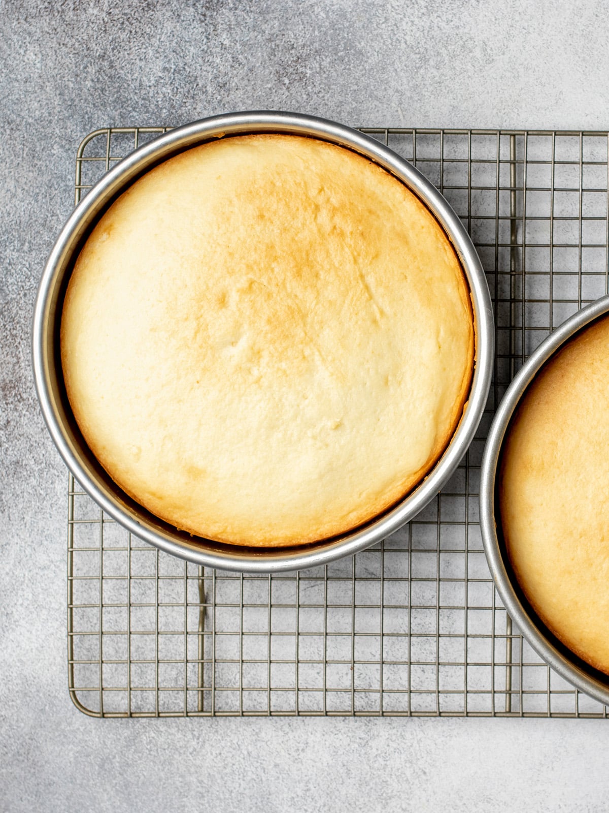 Overhead image of 2 yellow gluten free cakes in round metal baking pans on wire rack