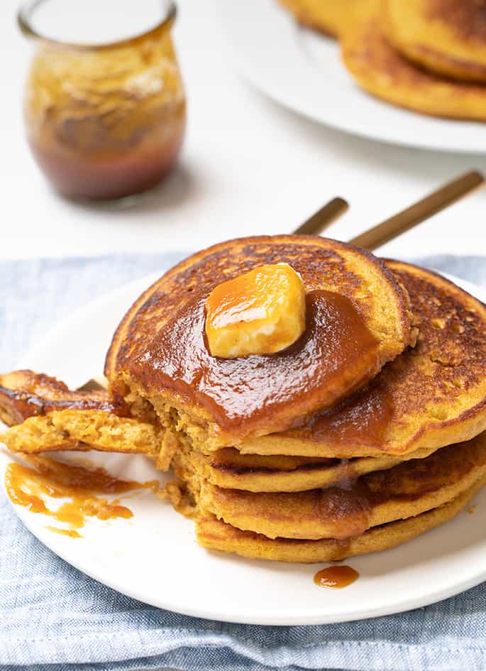 Stack of 5 pumpkin pancakes on white plate with pat of butter on top with bite on fork